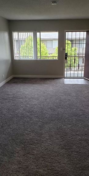 Downey apartment for rent - an empty living room with gray carpet and a glass door