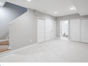 Philadelphia house for rent - A spacious room with white walls and flooring, featuring a staircase and a doorway leading to another room.