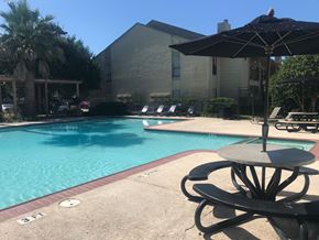 Houston apartment for rent - a swimming pool with a table and an umbrella in front of a building