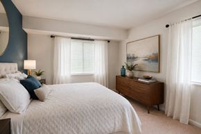 Alexandria apartment for rent - A bedroom with a large bed, a nightstand with a lamp, a dresser with a plant, and a painting on the wall.